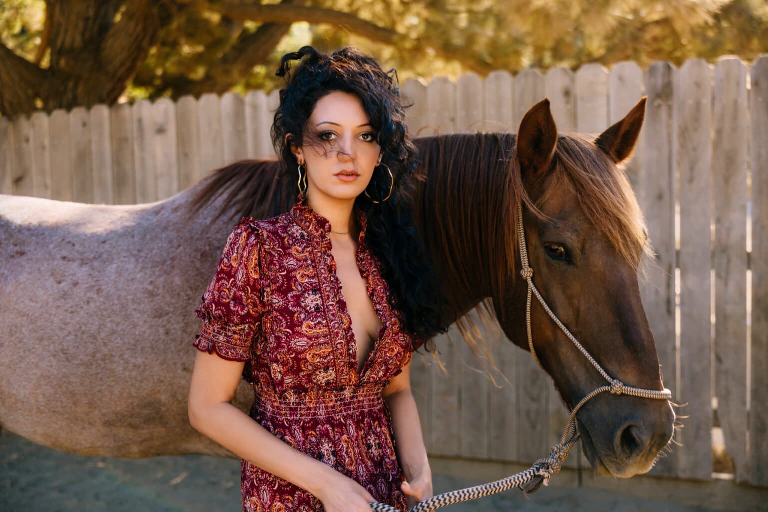 Fashion model posing outdoors beside a horse in a textured western setting