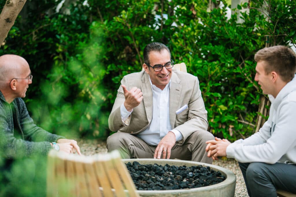 Businessmen chatting outdoors, smiling near a firepit for corporate headshots.