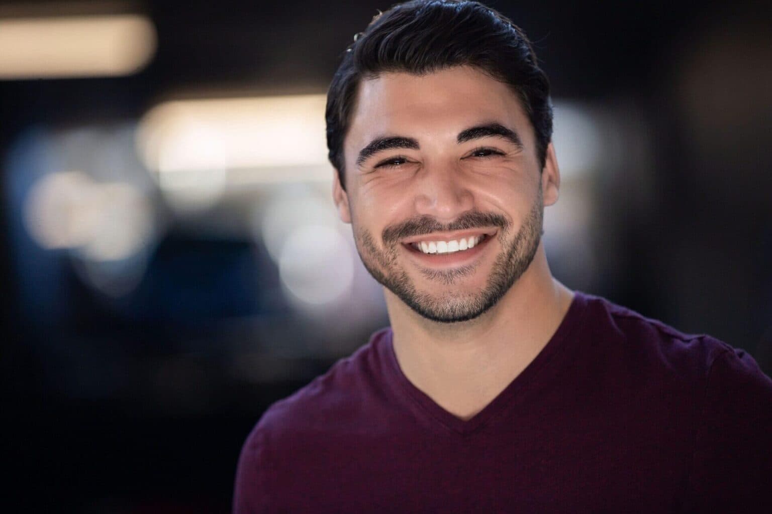 Smiling man with dark hair and beard, casual maroon shirt, professional headshot for agency.