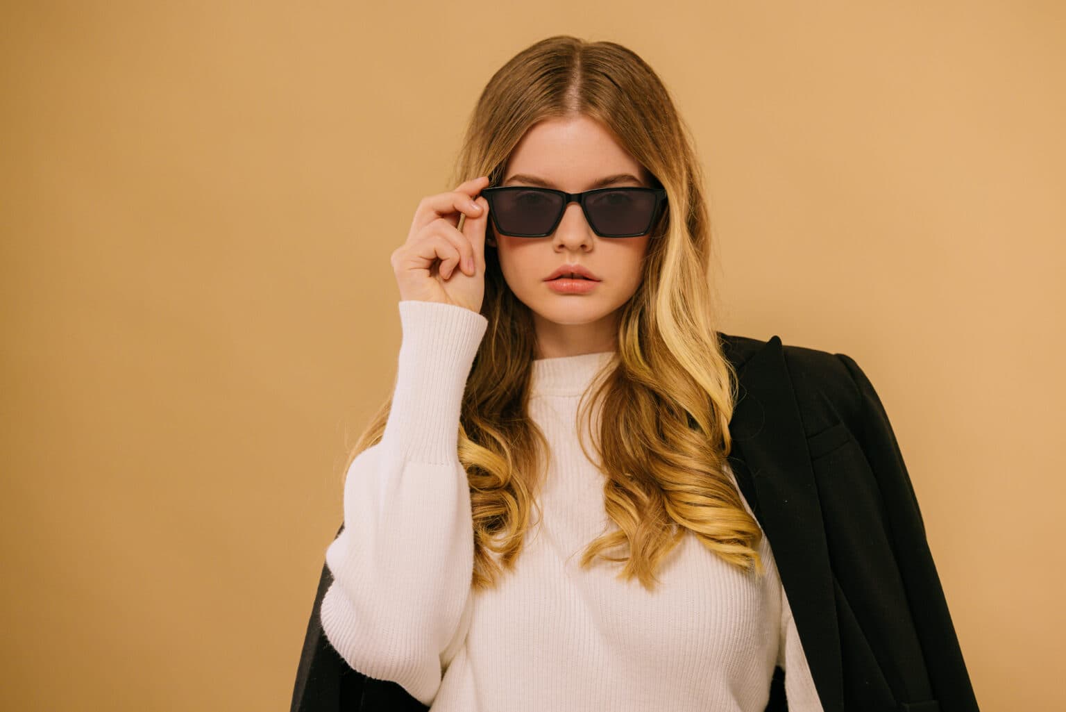 Blonde model posing in sunglasses against a warm neutral studio background