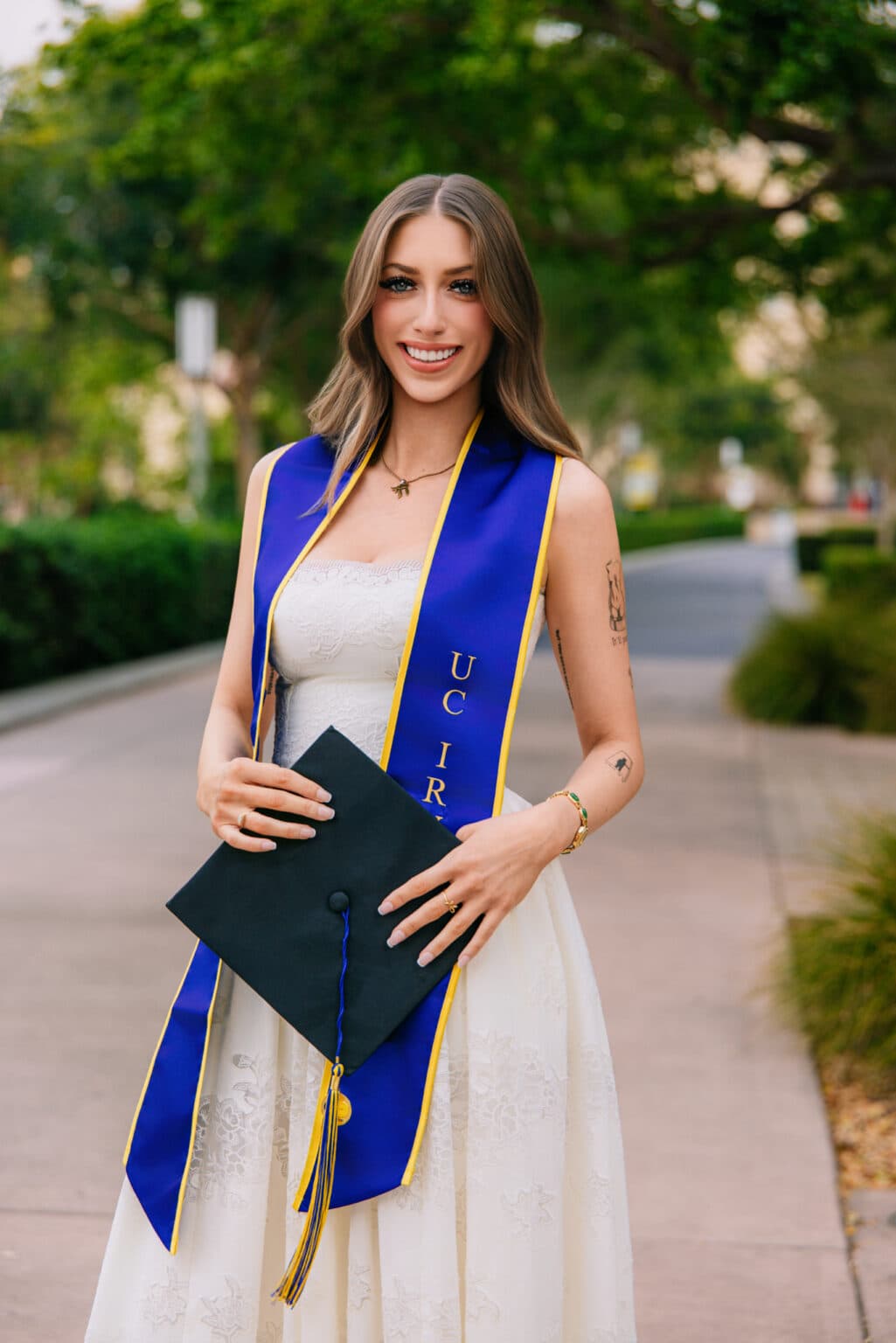 Female college graduate wearing a white dress and blue sash holding her graduation photography cap shoot in Southern California